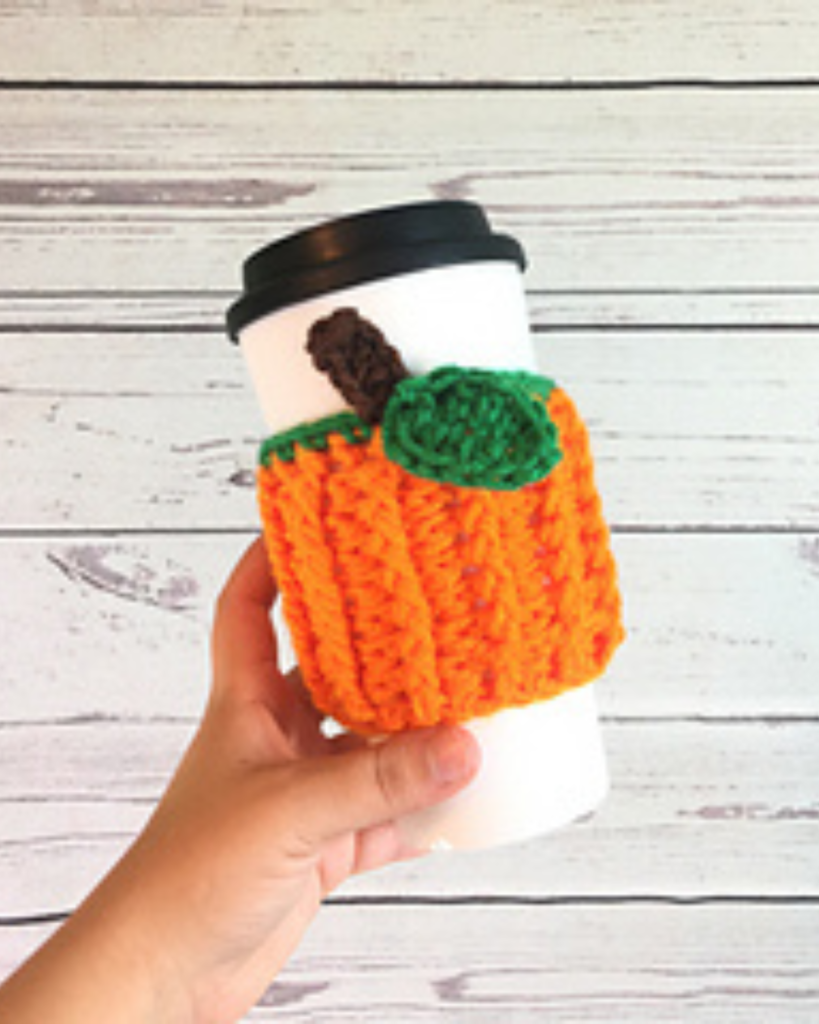 hand holding to go coffee with crochet pumpkin cozy
