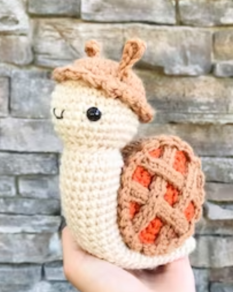 hand holding crochet snail with pumpkin pie shell