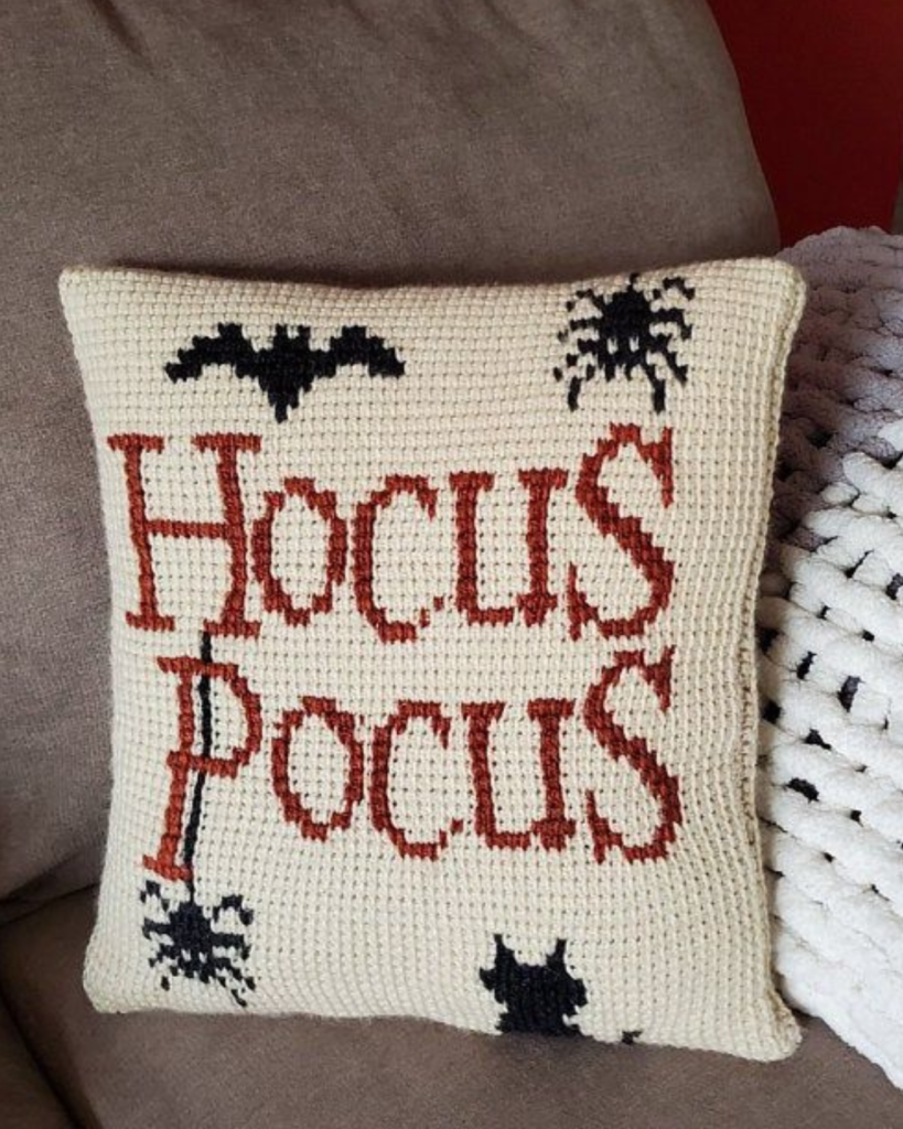 white crochet pillow case with spiders that says "Hocus Pocus"