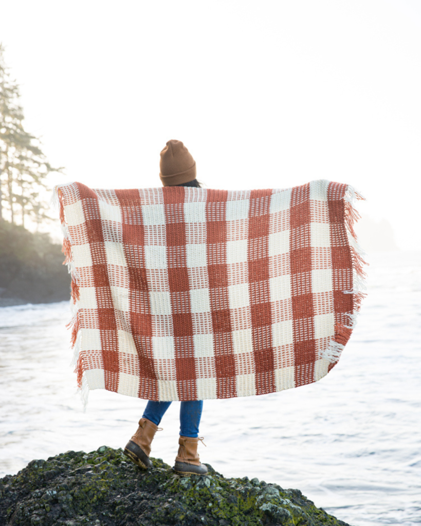 girl holding out white and orange crochet gingham blanket