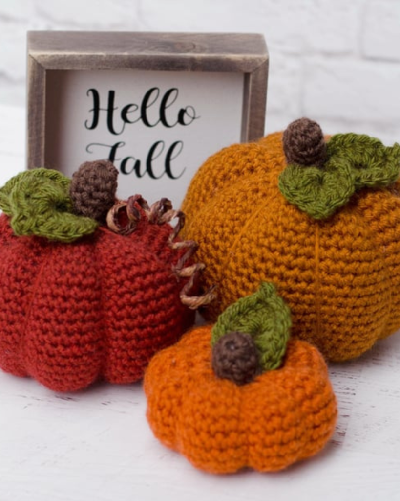 three crochet pumpkins of varying sizes, shapes, and colors