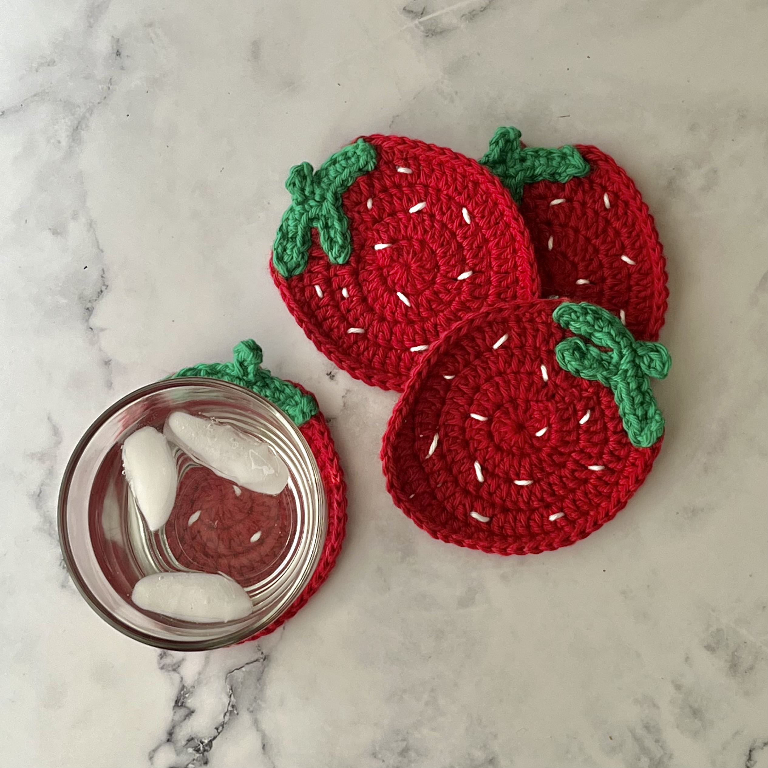 four red strawberry crochet coasters with cup of water
