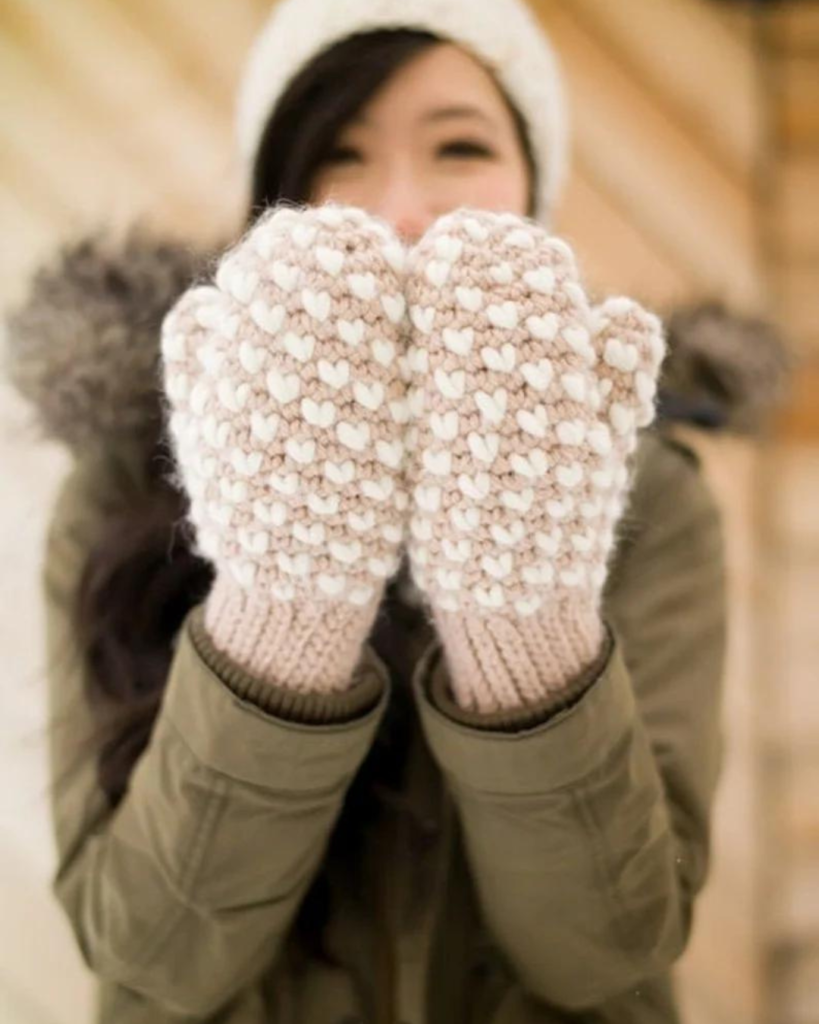 woman wearing tan crochet mittens with mini white hearts