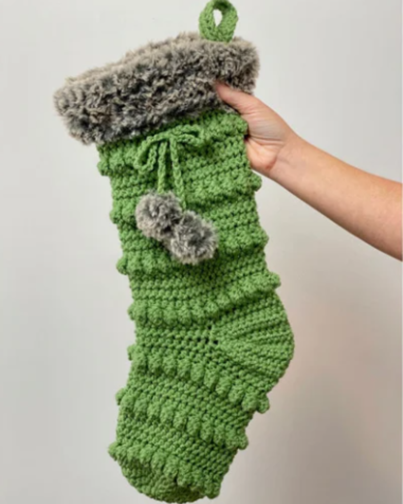 hand holding green bobble stitch crochet christmas stocking with fuzzy top