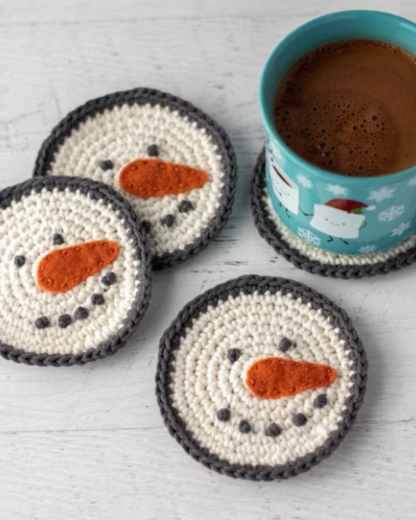 four crochet snowman coasters with hot chocolate