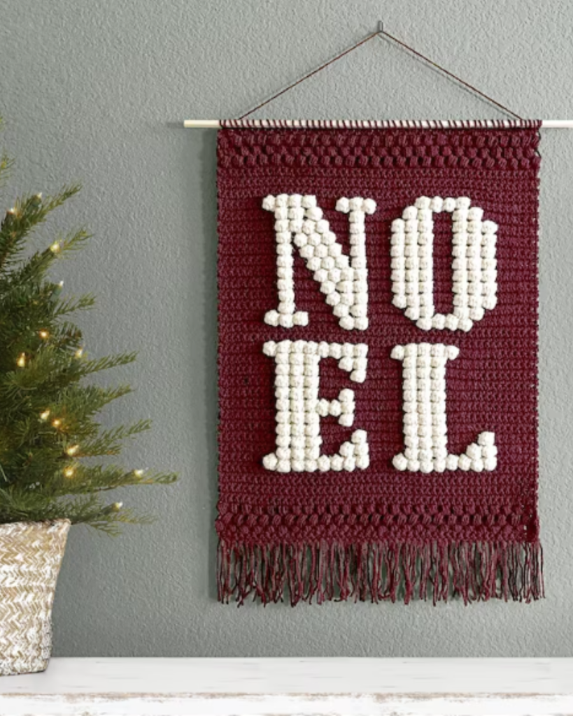 red and white crochet bobble wallhanging and reads "NOEL"