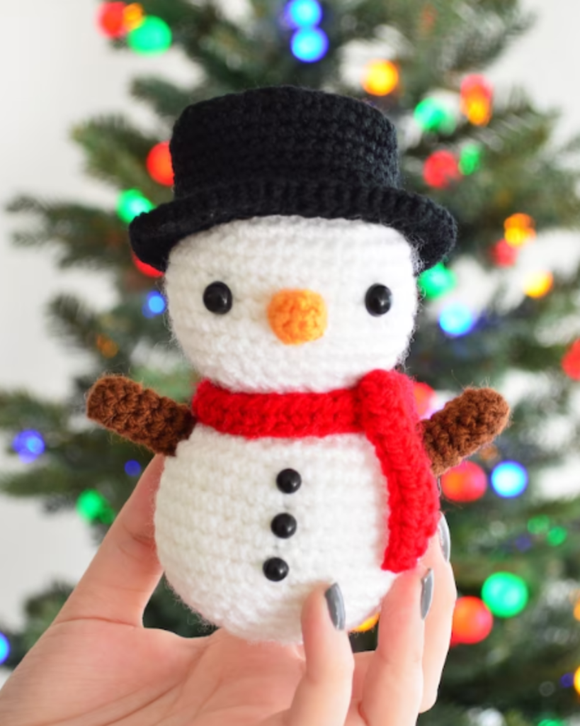 hand holding crochet snowman in front of christmas tree