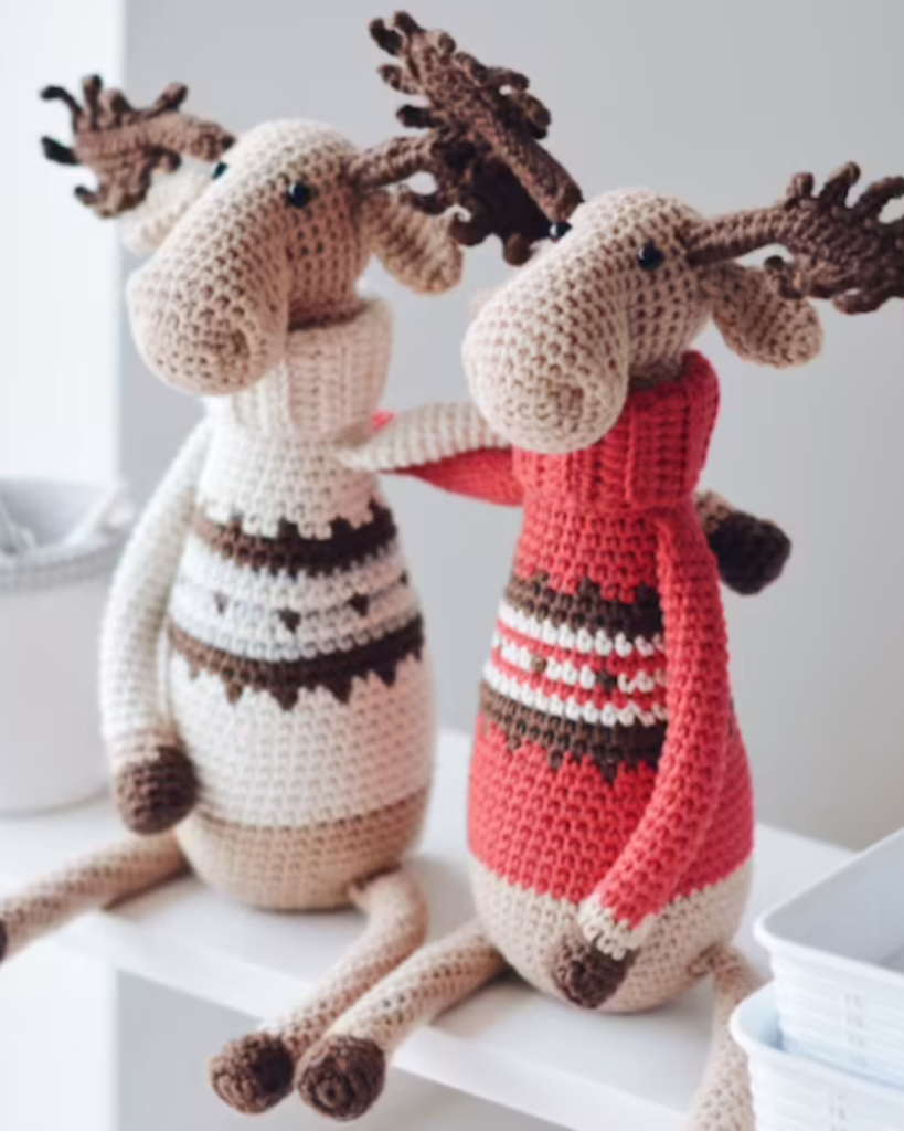 two crochet moose dolls wearing turtleneck sweaters