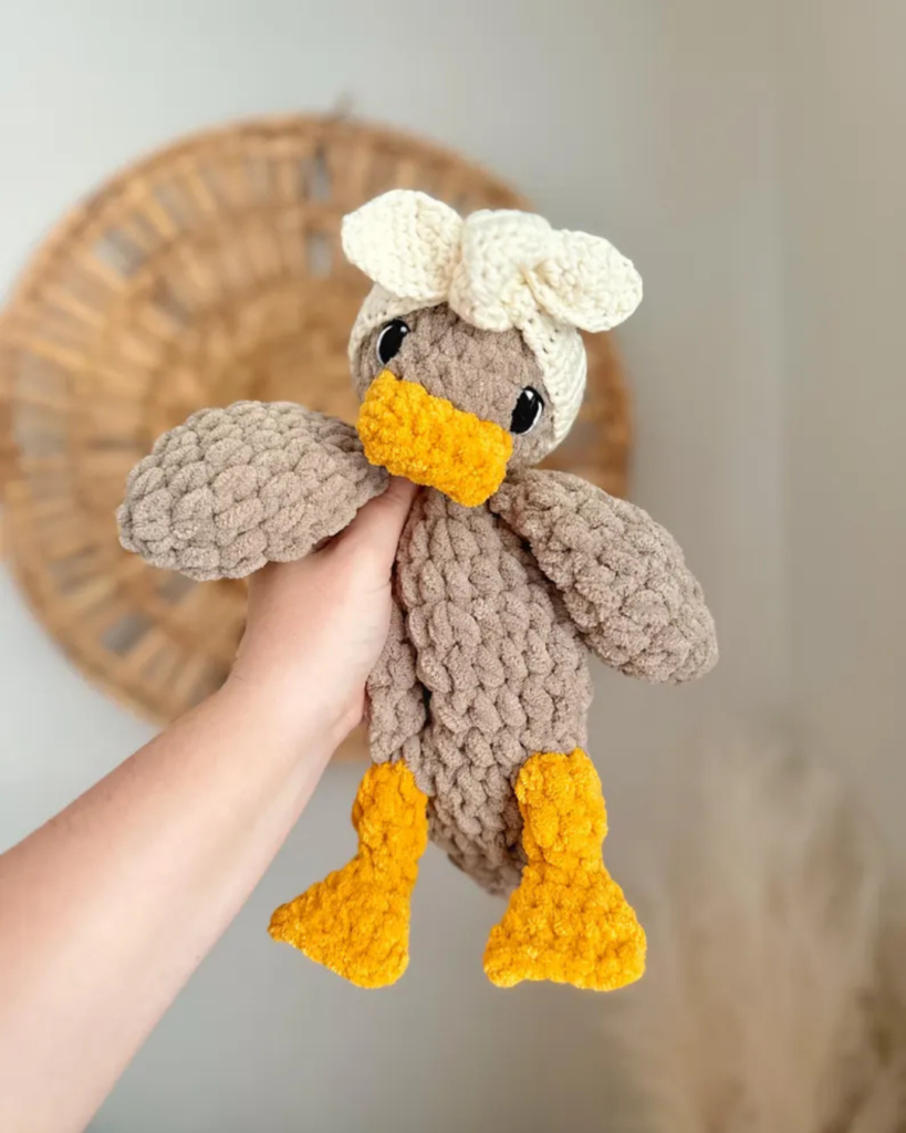 hand holding duck crochet snuggler wearing a tie headband