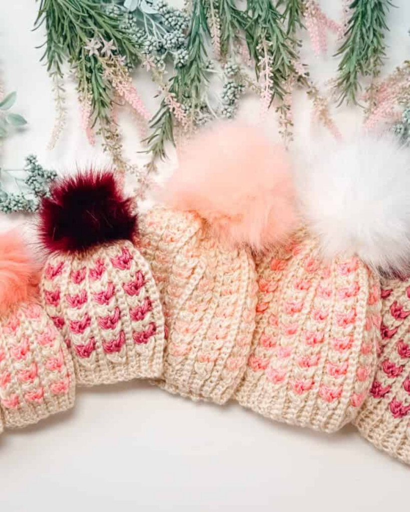 warm crochet baby hat in multiple sizes with heart details and a fluffy pom pom for winter