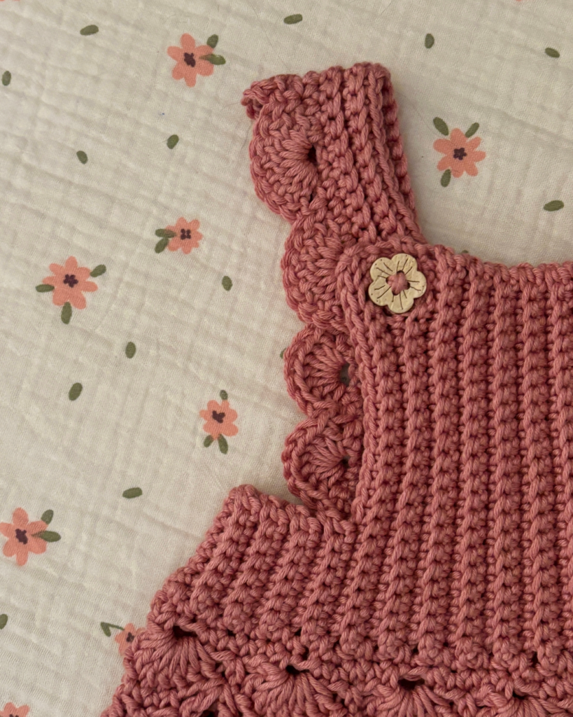 Front view of the Storybook Lane crochet baby overall dress showing the shell stitch skirt, ribbed bib, and wooden button straps.