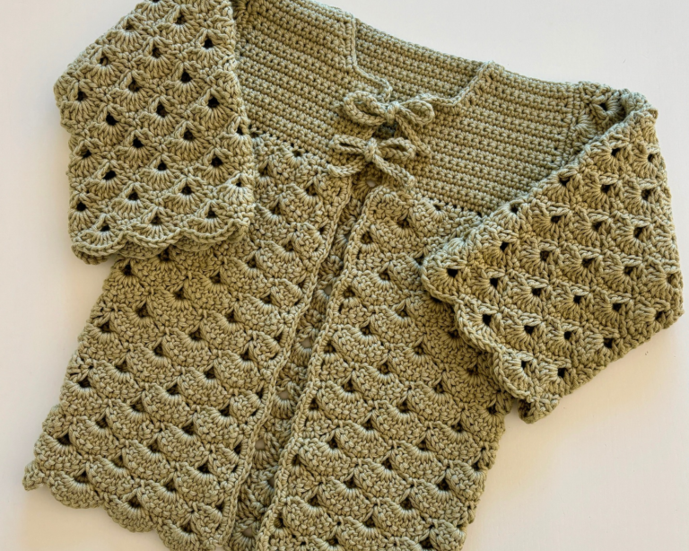 Crochet baby cardigan laid flat showing the shell stitch texture and bow closures