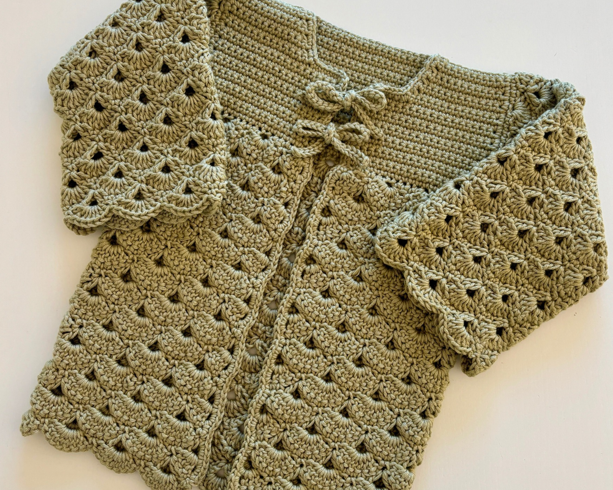 Crochet baby cardigan laid flat showing the shell stitch texture and bow closures