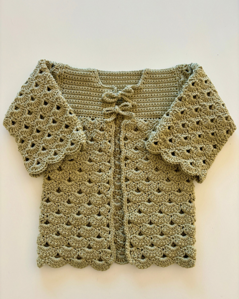 Crochet baby cardigan laid flat showing the shell stitch texture and bow closures