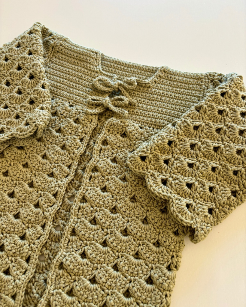 Front view of a crocheted baby cardigan featuring shell stitch and two bow ties