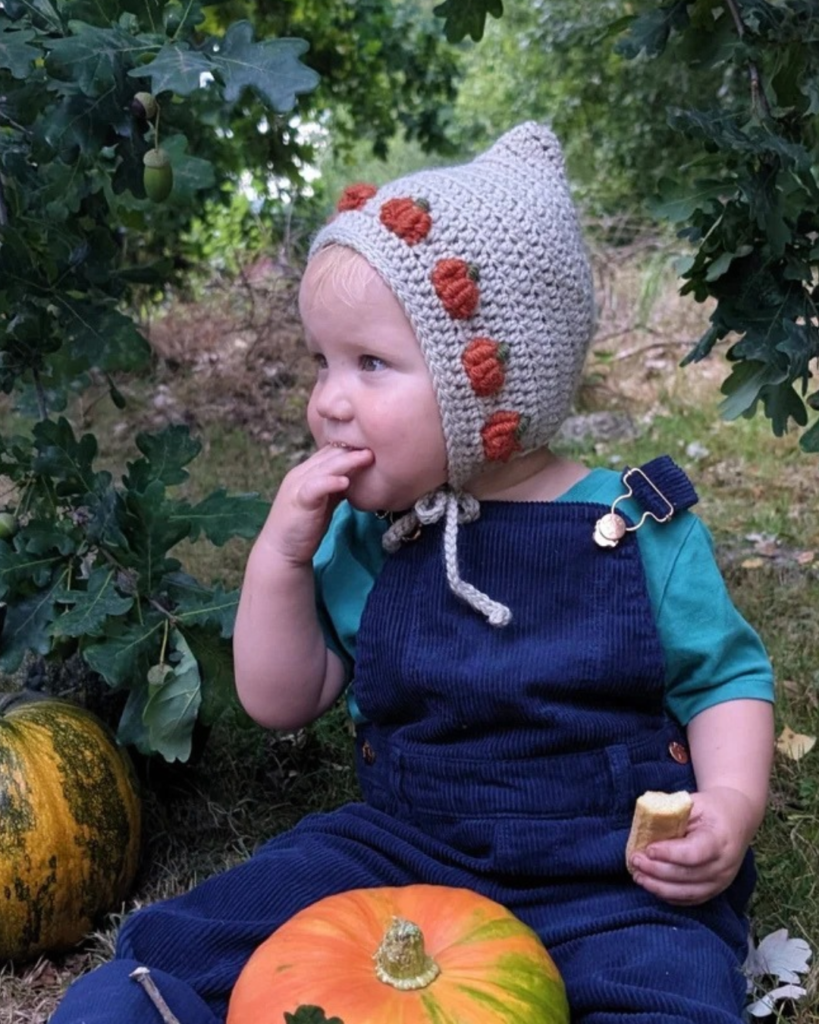 Crochet baby pixie bonnet with a pointed shape and small pumpkins along the crown.